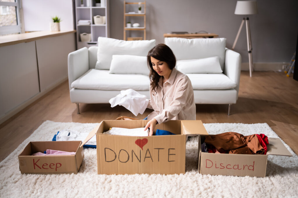 Woman decluttering and sorting items into keep-donate-discard boxes. 